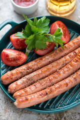 Grilled sausages with fresh parsley and tomatoes on a green serving pan, close-up, vertical shot