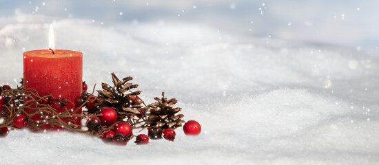 natural christmas decoration outdoors in snow, red burning candle with pine cones and berries...