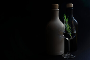 Tasty gin, white and black ceramic gin bottles with glass of gin and green rosemary on black...