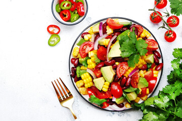 Mexican spicy salad with corn, red beans, avocado, jalapeno, tomatoes, onion and cilantro. White stone table background, top view