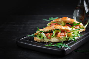 Croissants with salted salmon, cucumber and arugula served on dark background. Close up.