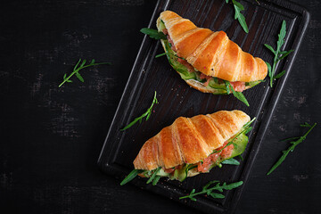 Croissants with salted salmon, cucumber and arugula served on dark background. Close up. Top view
