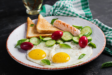 English breakfast - fried eggs, sausage, cucumber and toasts. American food.