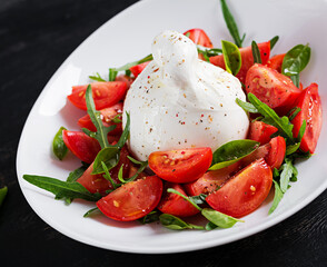 Salad with tomatoes and burrata cheese with basil and olive oil on plate. Italian food.