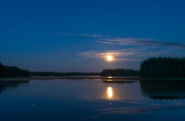 Moonlight night by the lake. Full moon and planet Jupiter in the sky and reflecting on water surface.