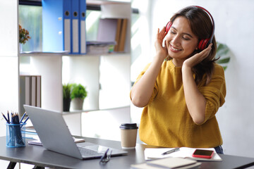 Woman wearing headphones working with laptop in the house and enjoying listening to music.