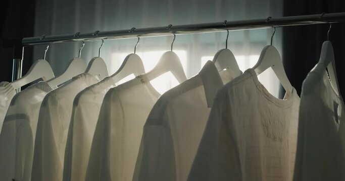 Rack with hangers of white clothes in the rays of the sun from the window