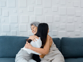 Portrait of happy Asian senior, mother or grandparent white hair embracing her beautiful daughter or grandchild smiling with love, care and comfort while sit on grey couch in living room at home.