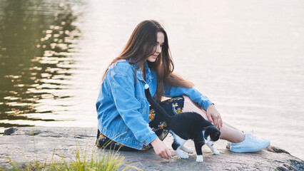 A girl plays with a cat by the lake.