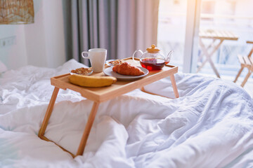 Tray with tasty breakfast in bed at light room in comfortable cozy morning