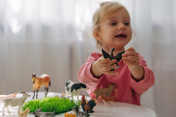 A little girl playing with farm animals on the table in nursery. Educational game. Learning through...