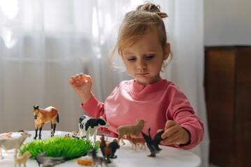 A little girl playing with farm animals on the table in nursery. Educational game. Learning through play. Montessori material concept for toddlers.