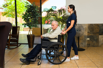 Old man on a wheelchair at the nursing home with a happy female nurse