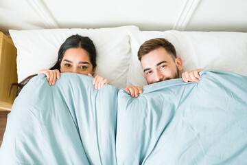 Fun couple waking up together under the covers in a comfy bed