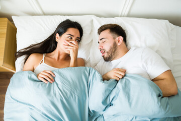 Annoyed woman suffering because of the bad breath of her husband in bed - obrazy, fototapety, plakaty