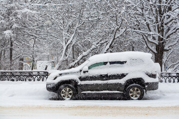 Snow-covered car on the street during a heavy snowfall. A lot of snow on the roadway, sidewalk, car...