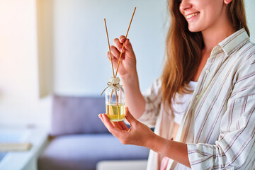 Young beautiful cute smiling satisfied girl holds in her hands a glass jar with wooden aroma sticks