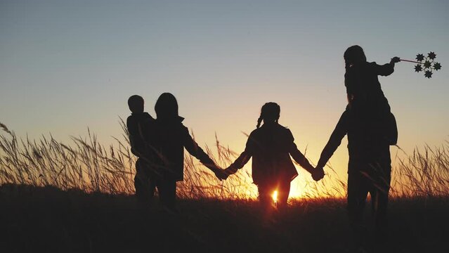 people in the park. happy family walk silhouette at sunset. mom, dad and daughters walk light holding a hands in park. concept of happy family childhood dream. parents and kids come back silhouette