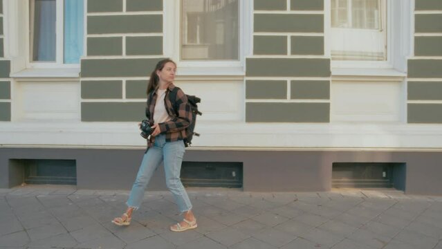 Female tourist takes photos with her camera while walking in cozy street of European small town. Young, carefree and relaxed caucasian woman on a vacation. 4k high quality footage