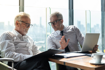 Two business men discussing idea in the office. One man is explaining while the other is listening. Both are wearing white shirt. The younger man is wearing tie and glasses.