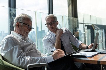 Two business men discussing idea in the office. One man is explaining while the other is listening. Both are wearing white shirt. The younger man is wearing tie and glasses.