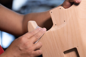 Craft man is rubbing sand paper against his wooden style electric guitar body