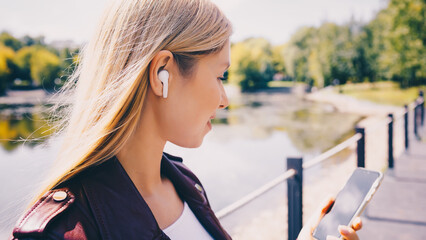 Young caucasian girl with wireless headphones in the park using tablet, phone and smiling