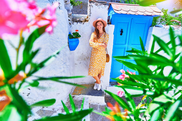 Girl traveler wearing dress and hat walks on an old beautiful street with white houses and blue doors in a European city