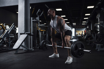 Fototapeta na wymiar Muscular bodybuilder lifting heavy barbell with an effort at gym