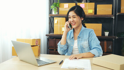 Obraz premium Online seller entrepreneur young asian woman using phone calling, checking online order. Woman calling check goods stock, delivery package shipping. Asian woman startup small business at home office