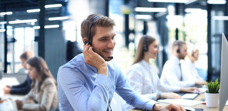 Portrait Of Call Center Worker Accompanied By His Team. Smiling Customer Support Operator At Work.