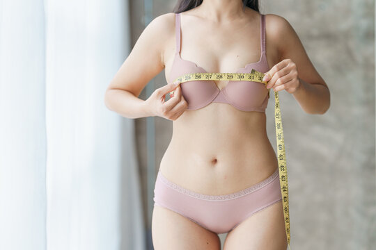 Close up pretty sexy asian woman slim body measuring breast for control weight loss and diet, indoors.