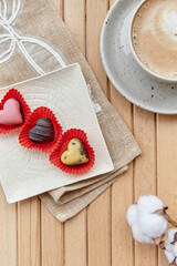 Atmosperic coffee time outside. Cup of cappuccino and bright chocolate sweets in shape of hearts. Romantic date, Valentines day