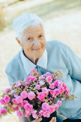 Portrait of smiling senior woman holding a purple flower pot outdoors