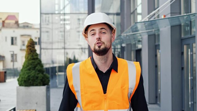 Professional male architect standing near modern glass building office and telling something on camera online or filming vlog. Businessman or architect telling details of project for customer or boss.