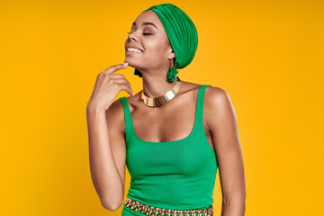 Attractive African woman in traditional headwear holding hand on chin against yellow background