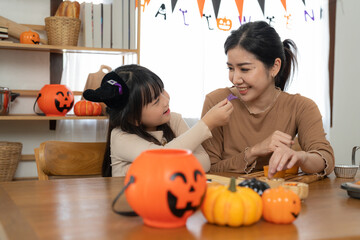 Happy smiling family mother and daughter making Halloween home decorations together while sitting at wooden table.