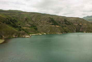 Obraz premium Mountain lake Gizhgit with beautiful turquoise water and high hilly shores on a cloudy summer day and a space for copying in the Elbrus region in the North Caucasus