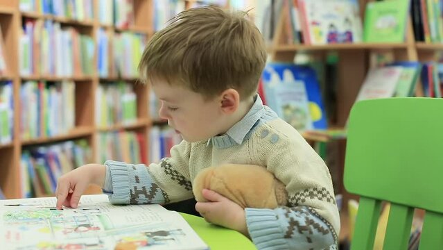 A little boy in the library is leafing through a children's picture book with interest. Selective focus
