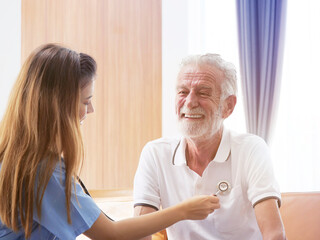 Fototapeta premium Health visitor talking to a senior man during home visit , Female caregiver doctor supporting smiling older man