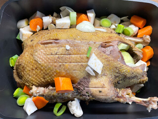 Vorgekochte Ente in einem Bräter mit dem Bruststück nach oben umgeben von kleingeschnittenem...