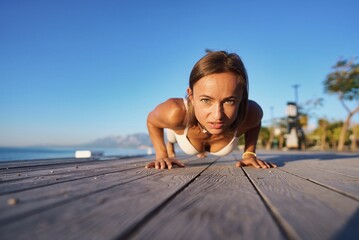 Fototapeta na wymiar Full length portrait of young athlete woman doing push ups on the deck. High quality photo