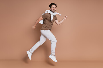 Fototapeta na wymiar Full length of fashionable young man running against brown background