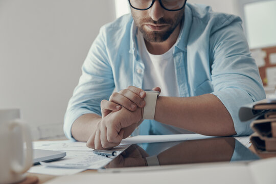 Close-up of young man looking at smart watch while sitting at his working place in office