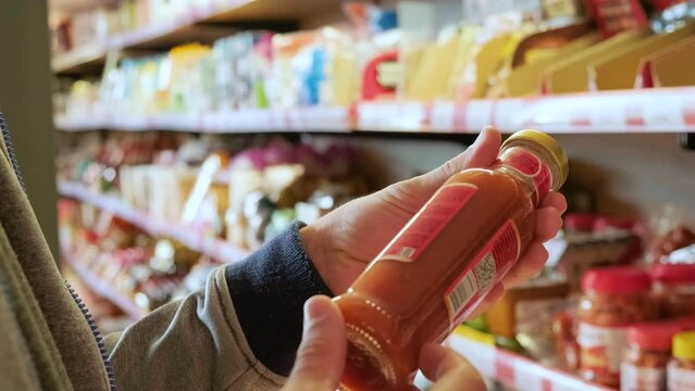 Close up of two male hands holding bottled product in store to read ingredients contents. Shopping concept. Conscious choice. 4k video
