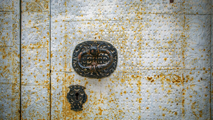 Old metal door with weathered black lock and knocker