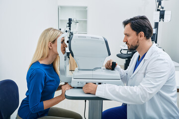Experienced ophthalmologist man using automated refractor for vision correction female patient in...