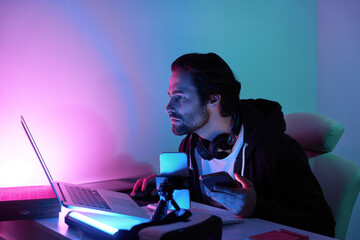 Confident young man using computer while streaming online against colorful background