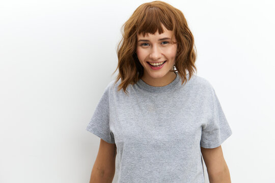 a happy, joyful woman in a gray cotton T-shirt stands against a light background, smiling happily and looking at the camera. Horizontal photo with an empty space for inserting an advertising layout