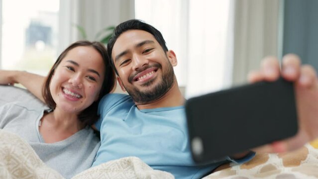 Asian couple, phone selfie or love bond in house living room or home interior sofa. Smile, happy and trust man and woman or boyfriend and girlfriend with mobile technology for social media photograph